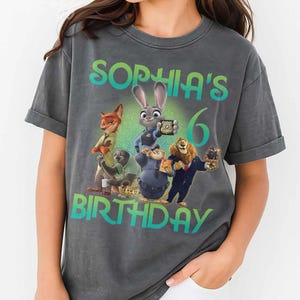 May include: Dark gray t-shirt featuring characters from the movie Zootopia, with the text "Sophia's 6th Birthday". The design includes Judy Hopps, Nick Wilde, and other characters. The word "Pepper" is printed at the bottom.
