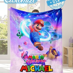 May include: A large, soft blanket featuring a vibrant illustration of Mario from "The Super Mario Galaxy" video game. The design includes Mario, various characters, and the text "MICHAEL" in colorful letters. The word "Customize" is also visible.
