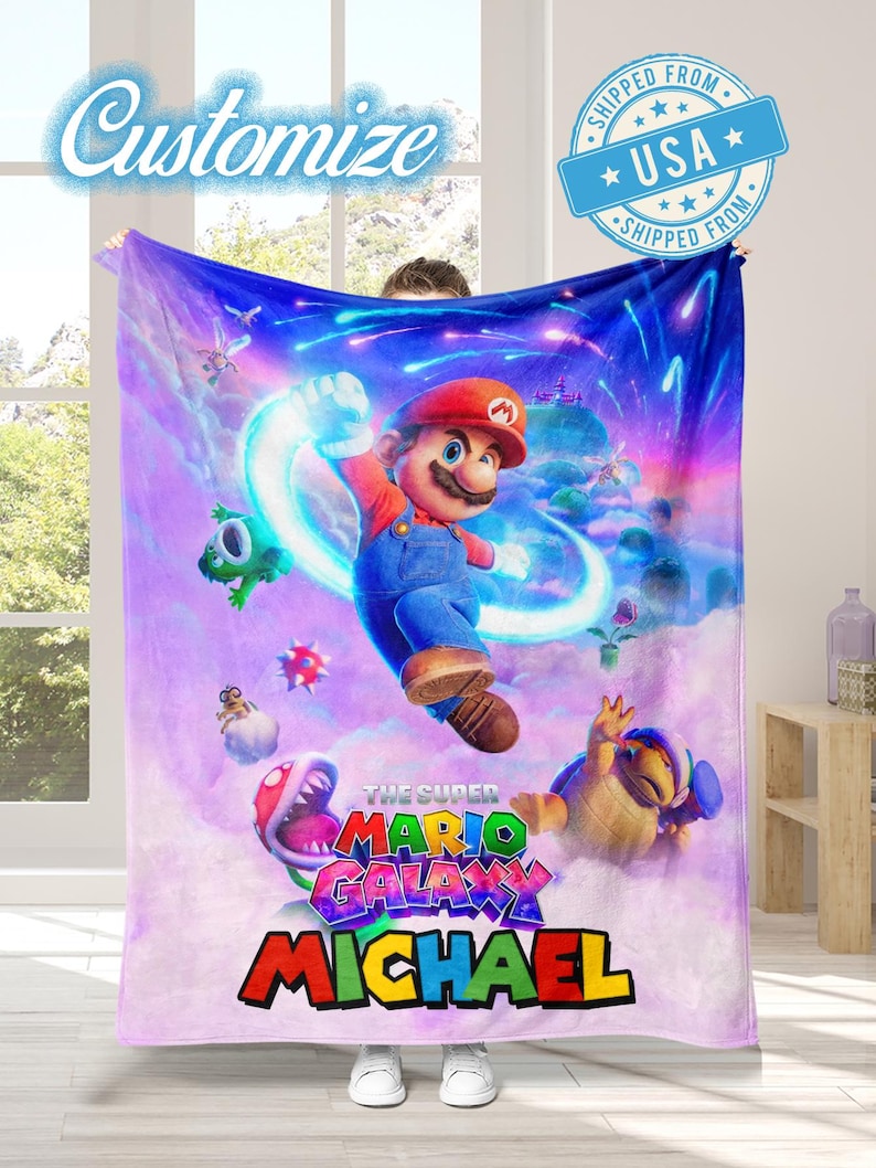 May include: A large, soft blanket featuring a vibrant illustration of Mario from "The Super Mario Galaxy" video game. The design includes Mario, various characters, and the text "MICHAEL" in colorful letters. The word "Customize" is also visible.