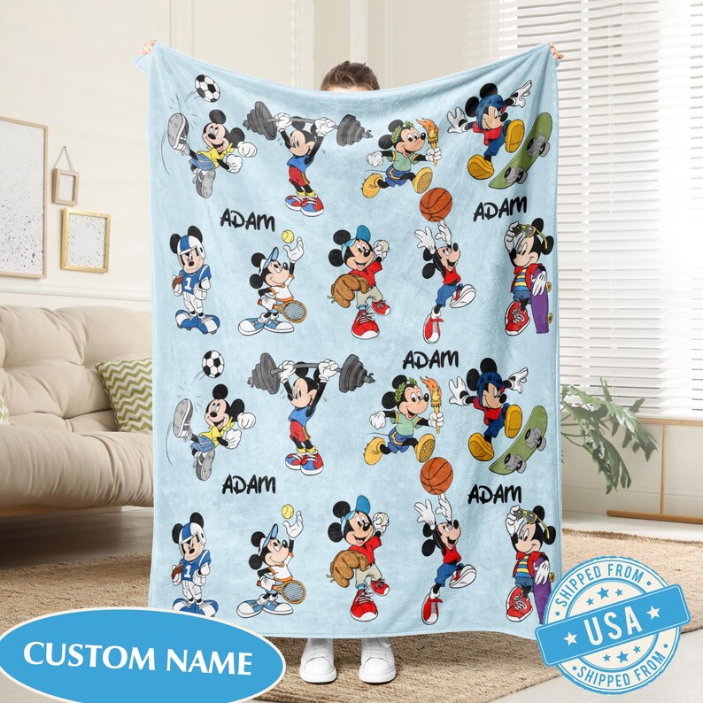 Puede incluir: Manta azul claro con un patr&oacute;n repetido de Mickey Mouse en varias poses deportivas. La manta tiene los nombres "ADAM" y "CUSTOM NAME" impresos. La manta est&aacute; hecha de un material suave.