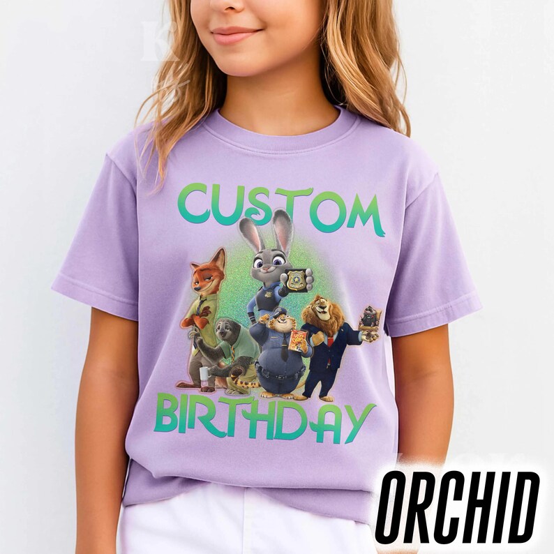 May include: A lilac-colored t-shirt featuring a group of animated characters with the words "CUSTOM BIRTHDAY" in green and blue. The word "ORCHID" is printed in black at the bottom right corner. The shirt is short-sleeved.