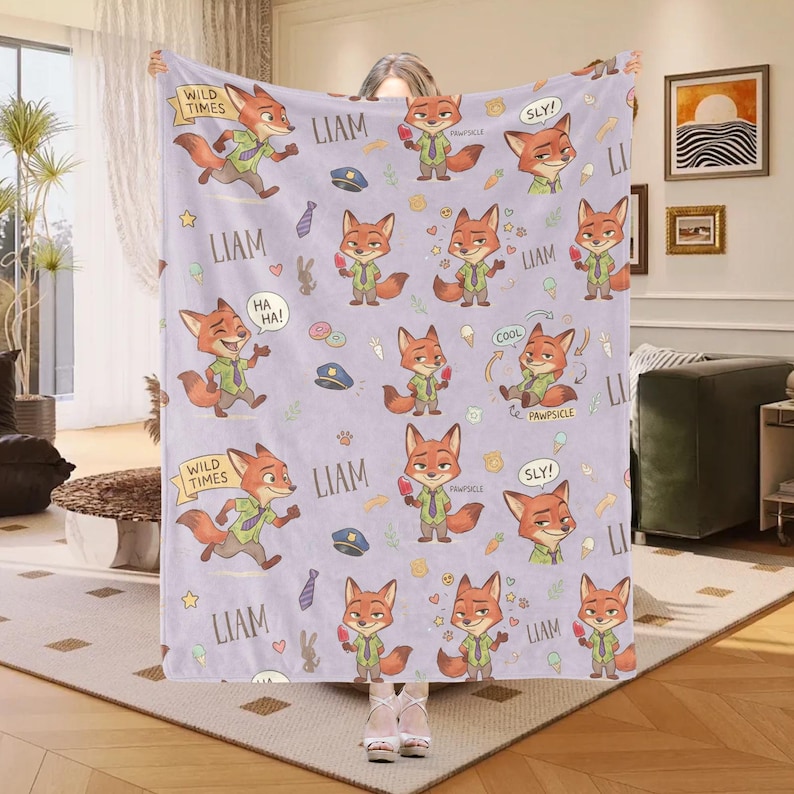 K&ouml;nnte beinhalten: Eine hellviolette Decke mit einem sich wiederholenden Muster eines Cartoon-Fuchses in verschiedenen Posen. Die Decke enth&auml;lt Texte wie "LIAM", "WILD TIMES", "HA HA!", "COOL" und "SLY!" sowie andere Cartoon-Elemente.