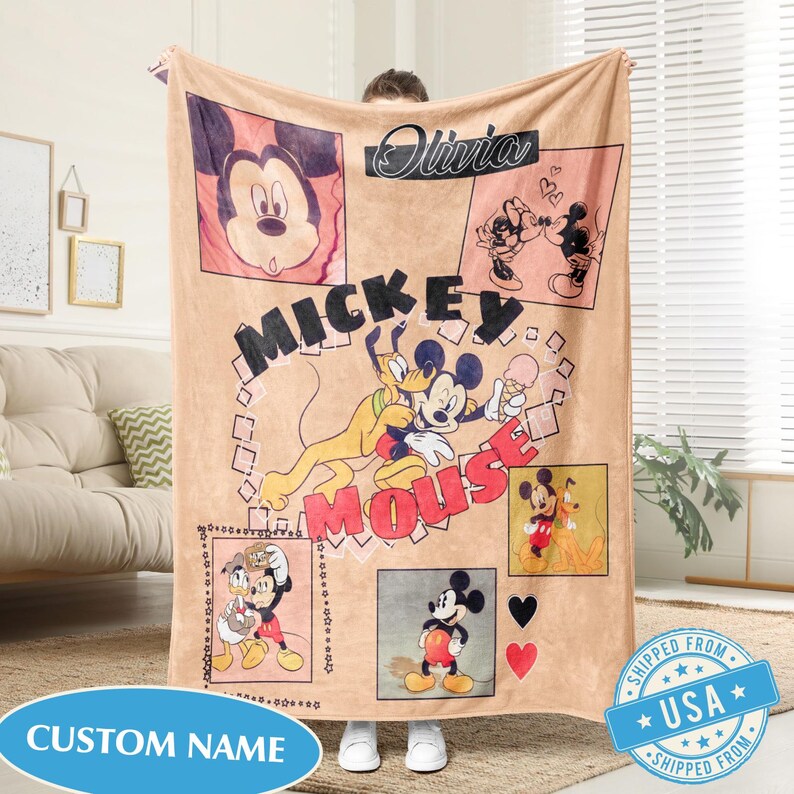 May include: A tan blanket featuring Mickey Mouse and Pluto illustrations. The blanket has the words "Mickey Mouse" in large letters, and the name "Olivia" in cursive. The blanket has a "Custom Name" label.