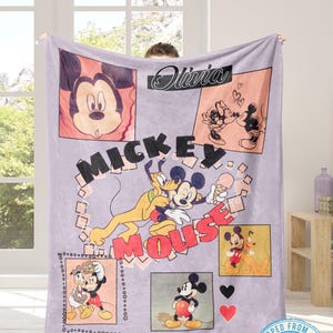 May include: A lavender Mickey Mouse blanket featuring multiple images of Mickey, Pluto, and Donald Duck. The blanket has the name "Olivia" in cursive and the words "Mickey Mouse" in large letters. The blanket is held up by a person.