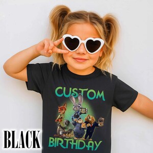 May include: Black t-shirt with a colorful graphic featuring characters from a cartoon movie. The shirt has the words "CUSTOM BIRTHDAY" in green and white. The child is wearing white heart-shaped sunglasses.