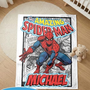 May include: A white blanket with a comic book cover design of Spider-Man. The blanket features a red, blue, and black colour scheme with the words "The Amazing Spider-Man" and a personalized name. The blanket is rectangular.