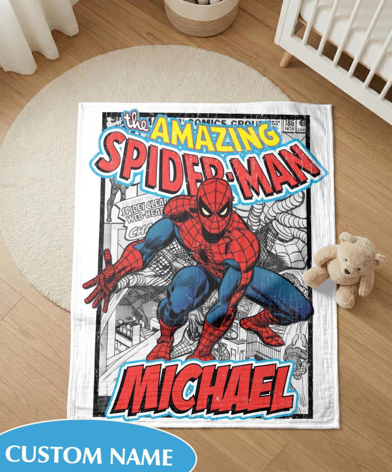 May include: A white blanket with a comic book cover design of Spider-Man. The blanket features a red, blue, and black colour scheme with the words "The Amazing Spider-Man" and a personalized name. The blanket is rectangular.