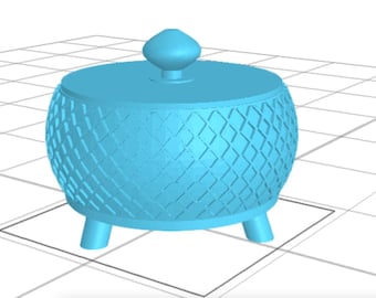 May include: A light blue decorative container with a lid and three small legs. The container has a textured, diamond-patterned exterior. The lid is topped with a small, rounded knob. The container is sitting on a grid.