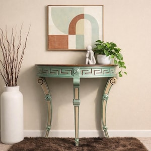 May include: A semi-circular console table with a distressed light green finish and a Greek key pattern along the apron. The table features three curved legs with cream-colored accents and a dark wood top, standing beside a tall white floor vase.
