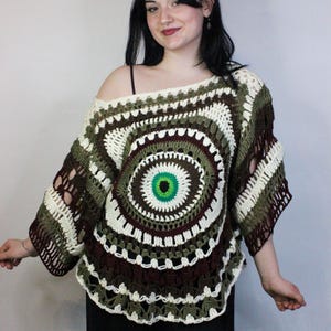 Puede incluir: Un top de ganchillo hecho a mano con un diseño asimétrico. El top presenta un patrón circular con tonos de verde, marrón y blanco. Las mangas son abiertas y el estilo general es bohemio.