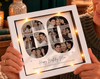 May include: A white square shadow box frame featuring a collage of photographs arranged in the shape of the number 60, illuminated by small LED lights. The text reads Happy Birthday Mum, THANK YOU FOR EVERTHING LOVE EMILY & TOM XXX.