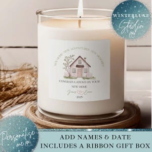 May include: A large white candle in a clear glass jar, with a lit wick. The label features a house illustration and the text "Congratulations on your new home." The candle sits on a wooden coaster. The text "Add names & date" is also visible.