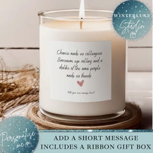 May include: A white candle in a clear glass jar with a lit wick. The candle has a label with the text "Chance made us colleagues. Sarcasm, eye rolling and a dislike of the same people made us friends." A small red heart is below the text.