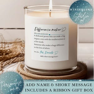 May include: A burning candle in a clear glass jar with a white label. The label says "Difference maker" with a definition and the name "Ms. Daniels". The candle is on a wooden coaster.