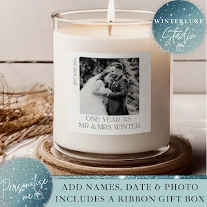 May include: A burning white candle in a clear glass jar. The candle features a label with a black and white photo of a couple, the text "ONE YEAR AS MR & MRS WINTER", and the date "21ST JUNE 2024". It rests on a wooden coaster.
