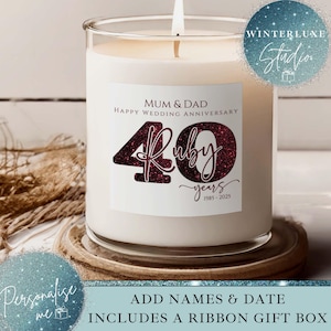 Könnte beinhalten: Eine weiße Kerze in einem Glas mit einer brennenden Docht. Das Etikett lautet "MUM & DAD HAPPY WEDDING ANNIVERSARY 40 Ruby years 1985-2025". Die Kerze steht auf einem Holzuntersetzer. Das Thema ist ein Hochzeitsgeschenk.