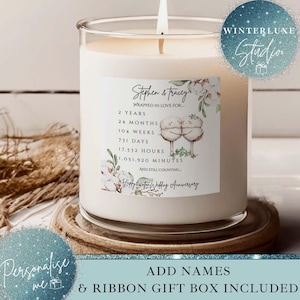 May include: A large, white scented candle in a clear glass jar. The candle has a label with the names "Stephen & Tracey" and a wedding anniversary message. The candle is on a wooden coaster.