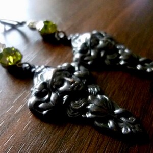 May include: Silver earrings with a detailed face design and green crystal accents.