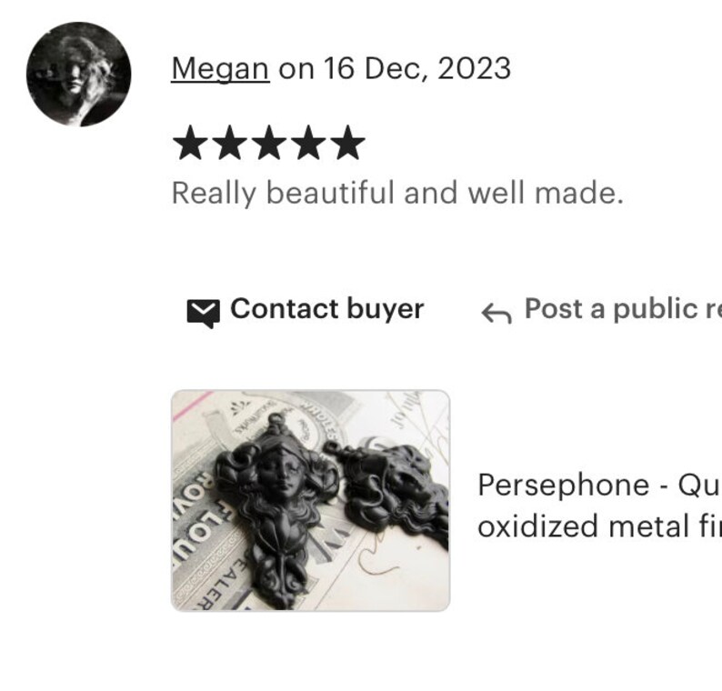 May include: Two black oxidized metal figures of a woman's head with long hair and a crown. The figures are on a piece of paper with writing on it. The text on the paper reads "Persephone - Queen of the Underworld".