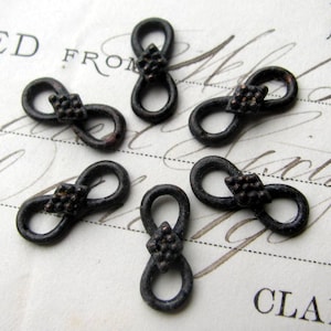 May include: Six black metal infinity loop clasps with a diamond-shaped accent in the center. The clasps are on a white surface with black writing.
