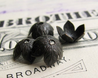 May include: Four black metal decorative end caps with a floral design. The end caps are on a white and black patterned surface.