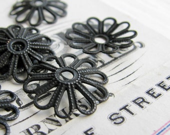 May include: Five black metal flower-shaped embellishments with intricate details. The embellishments are arranged on a white surface with black text.