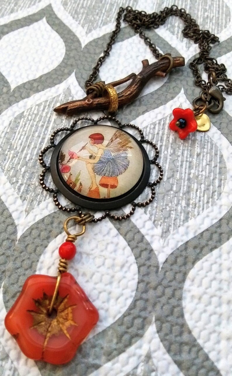May include: A necklace with a glass pendant featuring a fairy painting, a twig charm, and red glass flower accents.