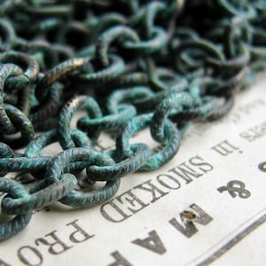 May include: A close-up of a chain made of metal links. The chain is a dark green color and has a textured surface. The chain is lying on a piece of paper with text that reads "A M & S SMOKED PRO"