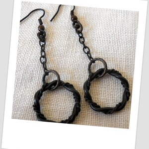 May include: A pair of black dangle earrings with a twisted wire design and a small wooden bead at the top of each earring.