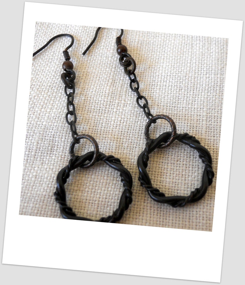 May include: A pair of black dangle earrings with a twisted wire design and a small wooden bead at the top of each earring.