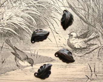 May include: Four black metal leaf-shaped charms with a textured surface. The charms are arranged on a vintage printed paper background with a bird illustration.