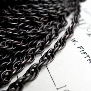 May include: Black chain with a twisted design. The chain is made of metal and has a dark, oxidized finish.