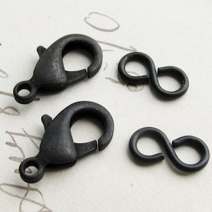 May include: Four dark gray metal jewelry clasps and connectors. Two are lobster claw clasps, and two are figure-eight connectors. The clasps have a spring-loaded mechanism for secure closure. The connectors are simple, looped designs.