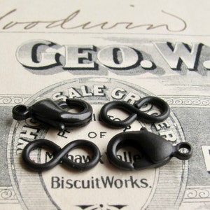 May include: Three black plastic clasps, two are lobster claw clasps and one is an infinity loop clasp. The clasps are on a vintage paper background.