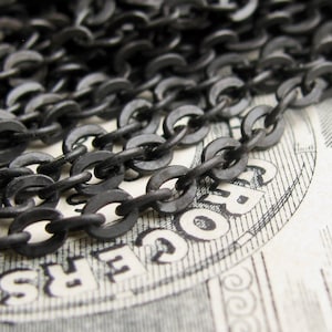 May include: Black chain necklace with a matte finish. The chain is made of metal and has a classic curb link design.