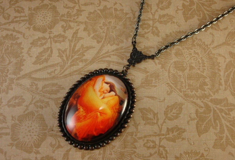 May include: A bronze necklace with a round cameo pendant featuring a painting of a woman in a red dress. The cameo is surrounded by a beaded border.