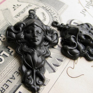 May include: Two black resin decorative embellishments with a woman's face and flowing hair. The embellishments are in the shape of a woman's head with a floral design.
