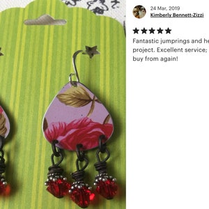 May include: A pair of dangle earrings with a floral pattern on the metal charm and red glass beads hanging from the bottom.