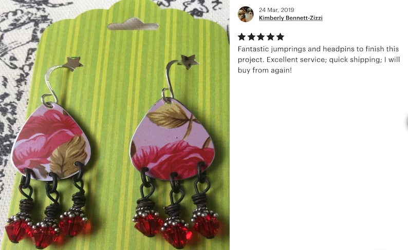 May include: A pair of dangle earrings with a floral pattern on the metal charm and red glass beads hanging from the bottom.