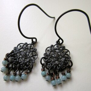 May include: A pair of black filigree earrings with light blue gemstone accents. The earrings feature a delicate, intricate design and dangle from a simple hook.