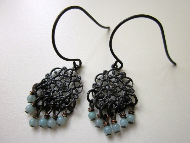 May include: A pair of black filigree earrings with light blue gemstone accents. The earrings feature a delicate, intricate design and dangle from a simple hook.