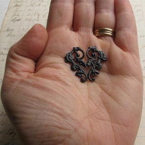 May include: A black metal heart-shaped design with intricate floral details. The design is made of metal and has a black finish.