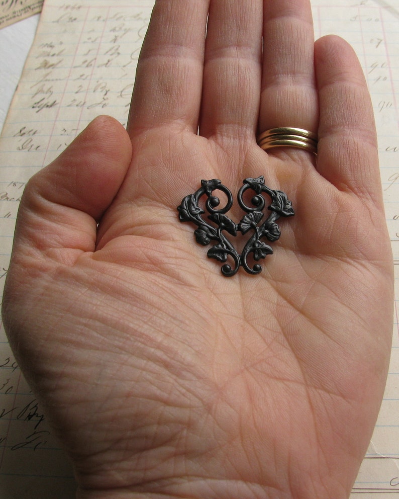 May include: A black metal heart-shaped design with intricate floral details. The design is made of metal and has a black finish.