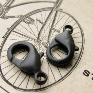 May include: Two black metal lobster clasps, also known as trigger snaps, are shown on a white background with a vintage bicycle illustration. The clasps are a common jewelry finding used for attaching chains, cords, and other jewelry components.