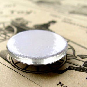 May include: A white round button with a silver metal rim. The button is blank and ready to be customized.