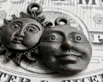 May include: Two antique-style metal charms, one depicting a sun with a face and the other a moon with a face. Both charms are in a dark bronze color.