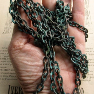 K&ouml;nnte beinhalten: Nahaufnahme einer langen, dicken Kette aus Metallgliedern. Die Kette ist dunkelbraun mit einer gr&uuml;nen Patina. Die Kette liegt auf einer Hand.