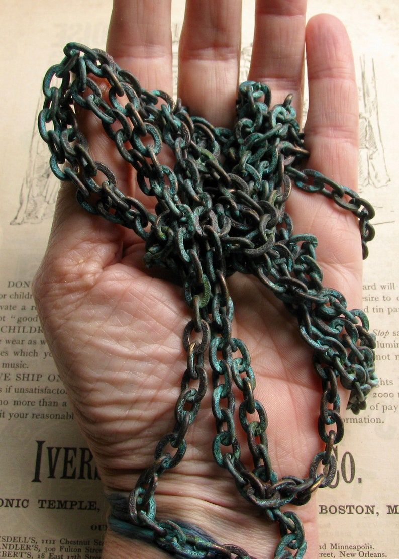 K&ouml;nnte beinhalten: Nahaufnahme einer langen, dicken Kette aus Metallgliedern. Die Kette ist dunkelbraun mit einer gr&uuml;nen Patina. Die Kette liegt auf einer Hand.