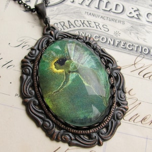 Op de afbeelding: Een bronzen hanger met een sierlijk frame en een groene glazen cameo met een fee met gloeiende vleugels.