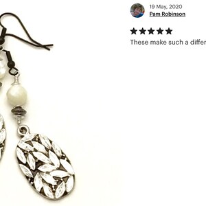 May include: Silver earrings with white oval beads and a leaf design. The earrings have a hook closure.
